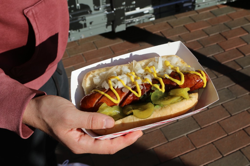 Grilled sausage sandwich with onions, mustard, and pickles in a paper boat