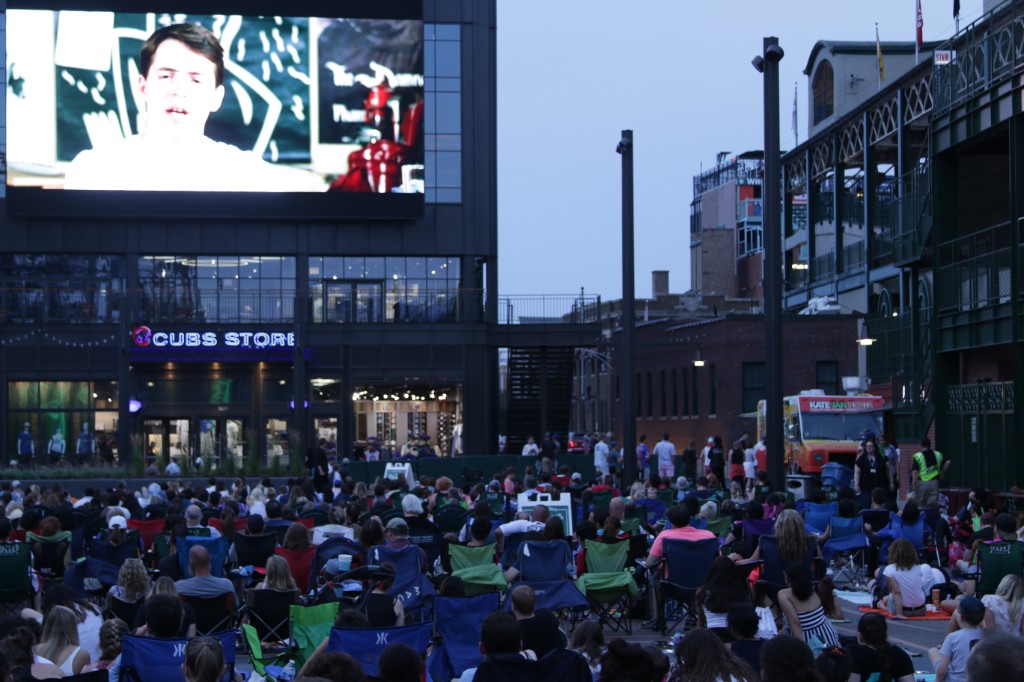 Moviegoers on the lawn facing the giant screen above the Cubs Store on Gallagher Way