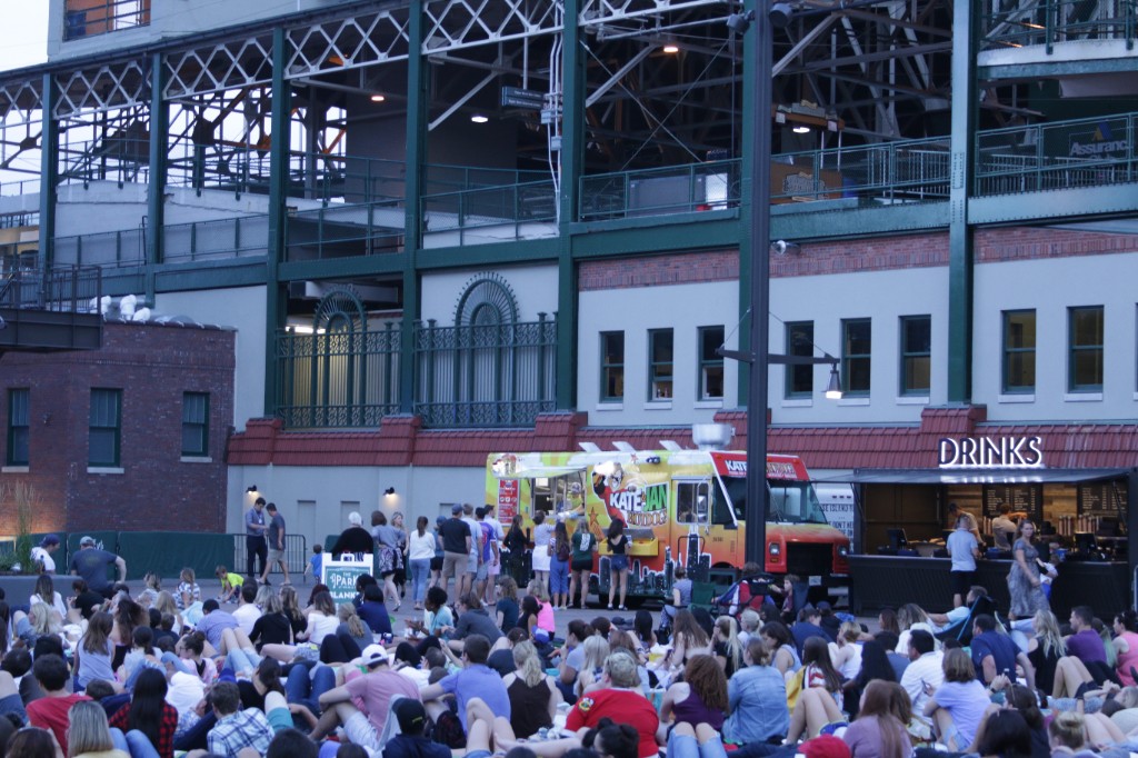 Moviegoers fill the lawn while a film plays on the big outdoor screen at Gallagher Way